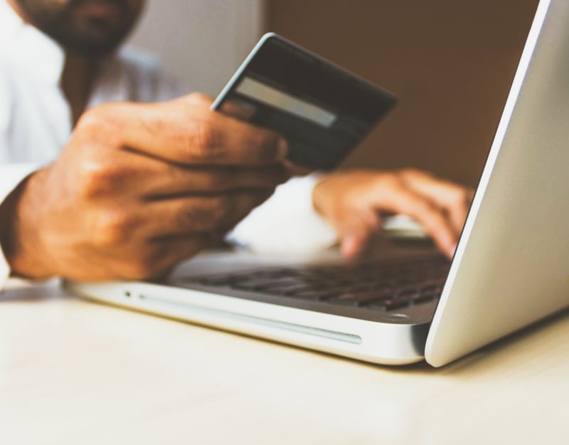 Picture of a hand holding a credit card in front of a PC
