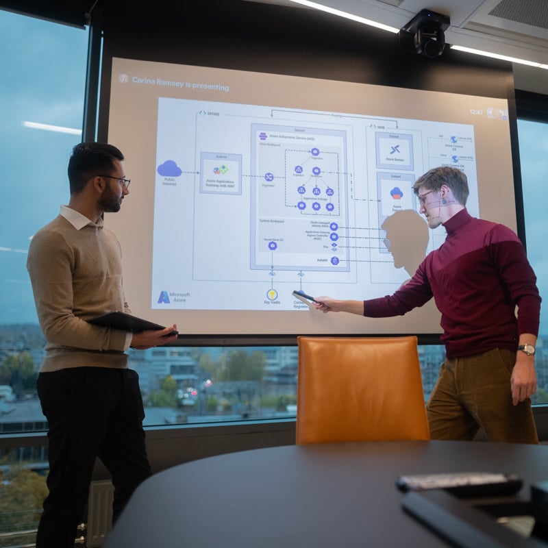 Two men standing in front of a screen lookling at data