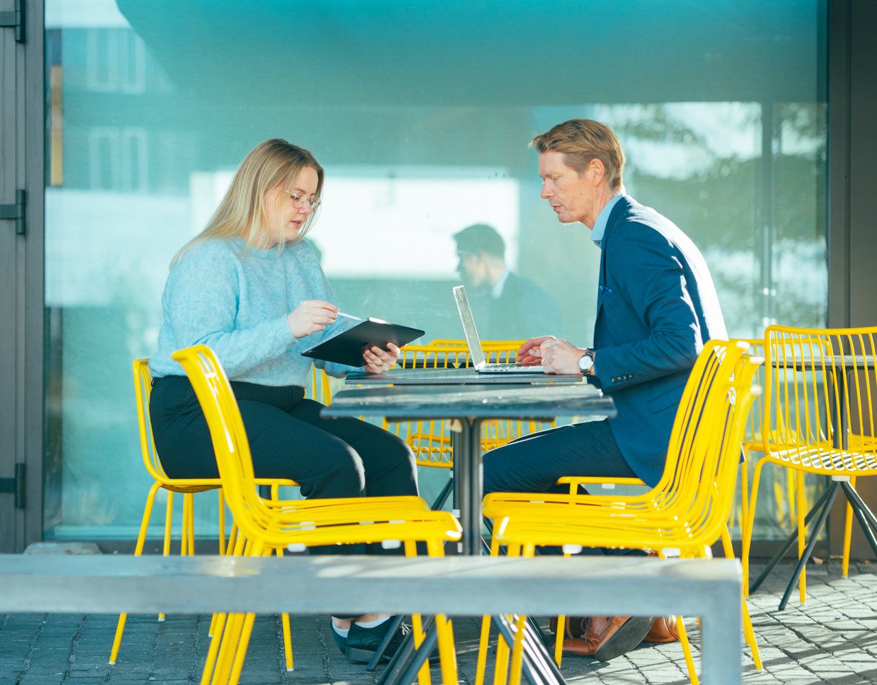 A woman and a man are sitting in a cafe with yellow chairs and working.