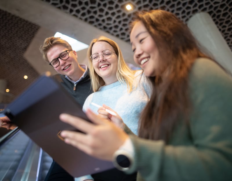 Three persons are smiling and looking on an iPad