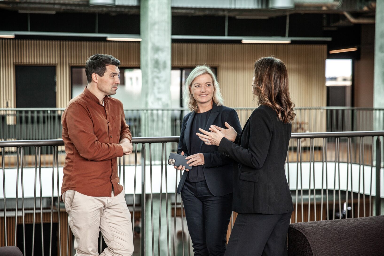 Three colleagues stand chatting by a staircase.